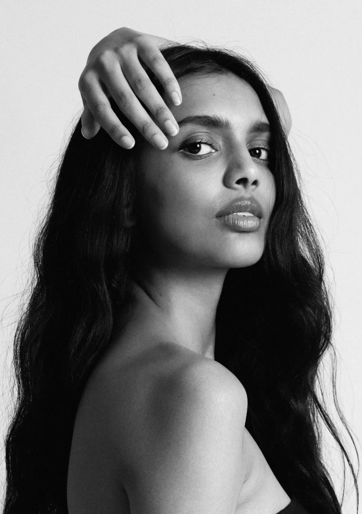 Black and white: model with long dark hair, hand pressed to her head, looking down and to the side