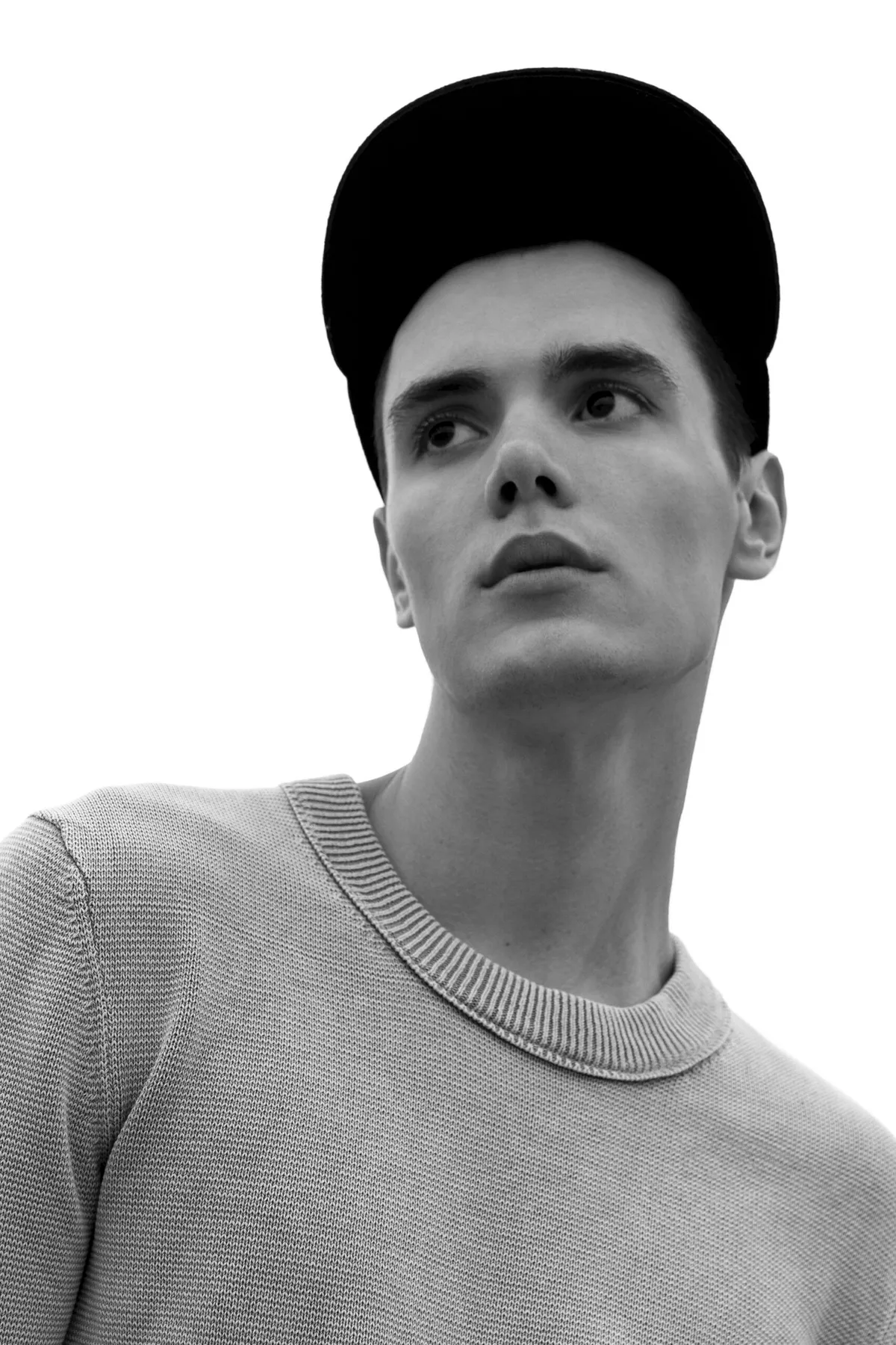 Black and white: man in a cap and knit sweater looking up, on a white ground