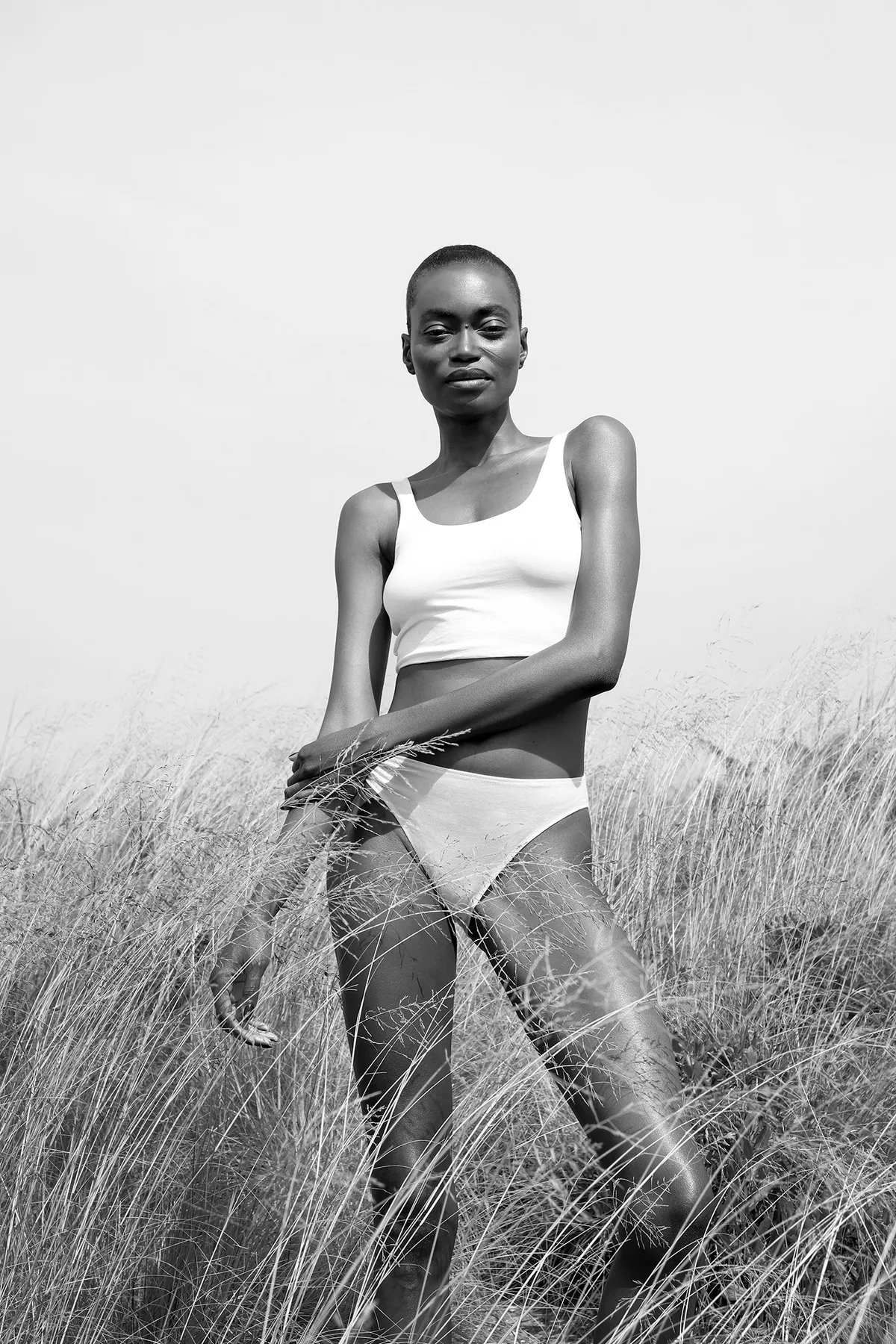 Model in a white crop top and brief walking through pale grass, black and white