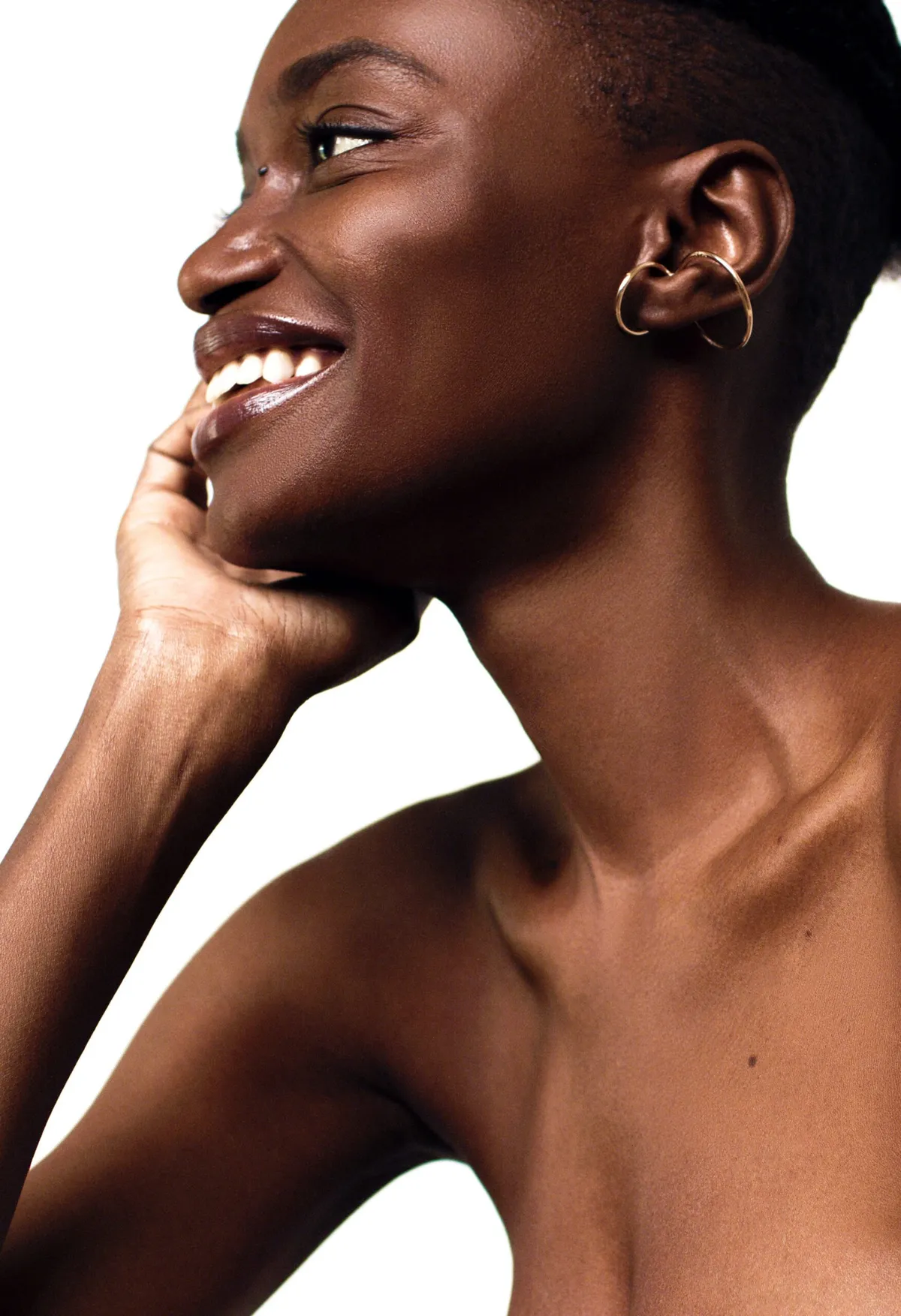 Profile of a model laughing, chin resting on her hand, a gold hoop earring catching the light