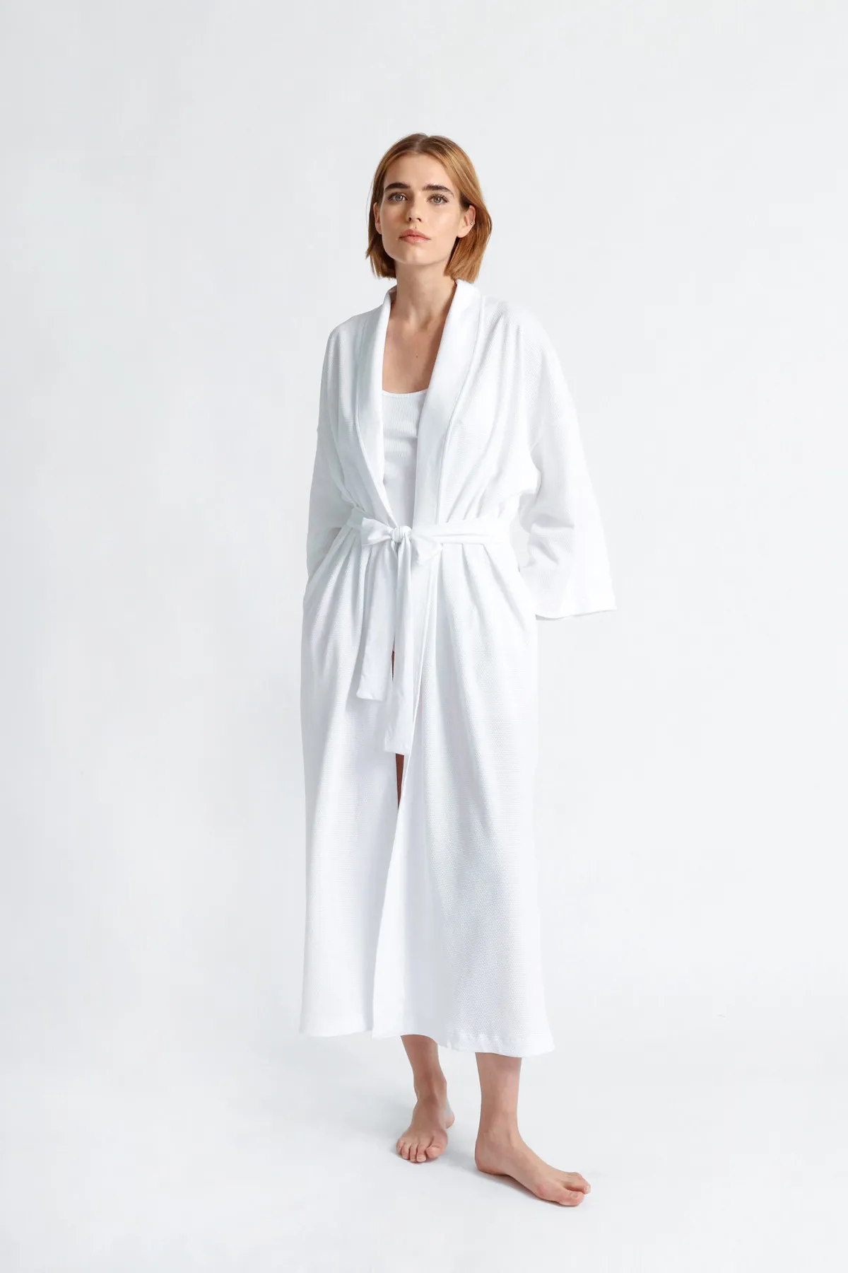 Full-length: model in a long white wrap robe, barefoot, on a white ground