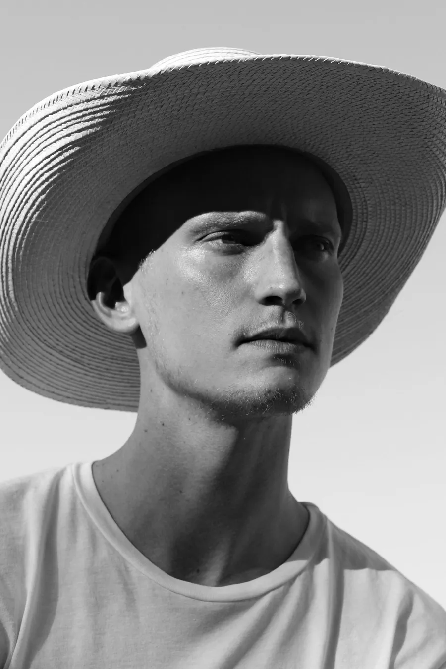 Black and white profile of a man in a wide-brimmed straw hat and white tee